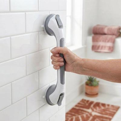 A senior person using a chrome suction grab bar on a glossy white tiled bathroom wall for safety and stability.